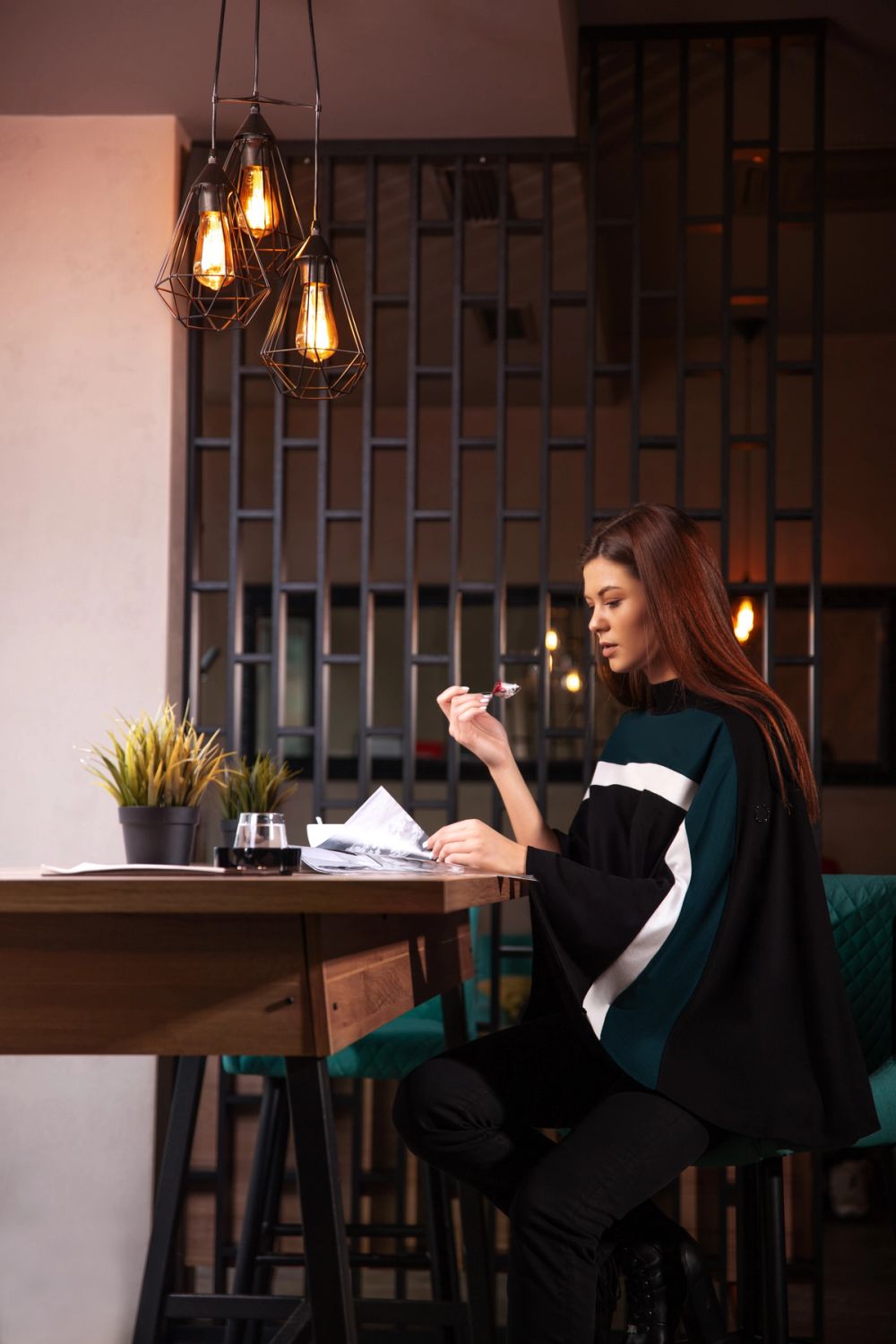Model u modernom outfitu sedi u elegantnom enterijeru restorana, fotografisana u ambijentalnom svetlu, sa fokusom na stil, atmosferu i lifestyle modni kontekst.