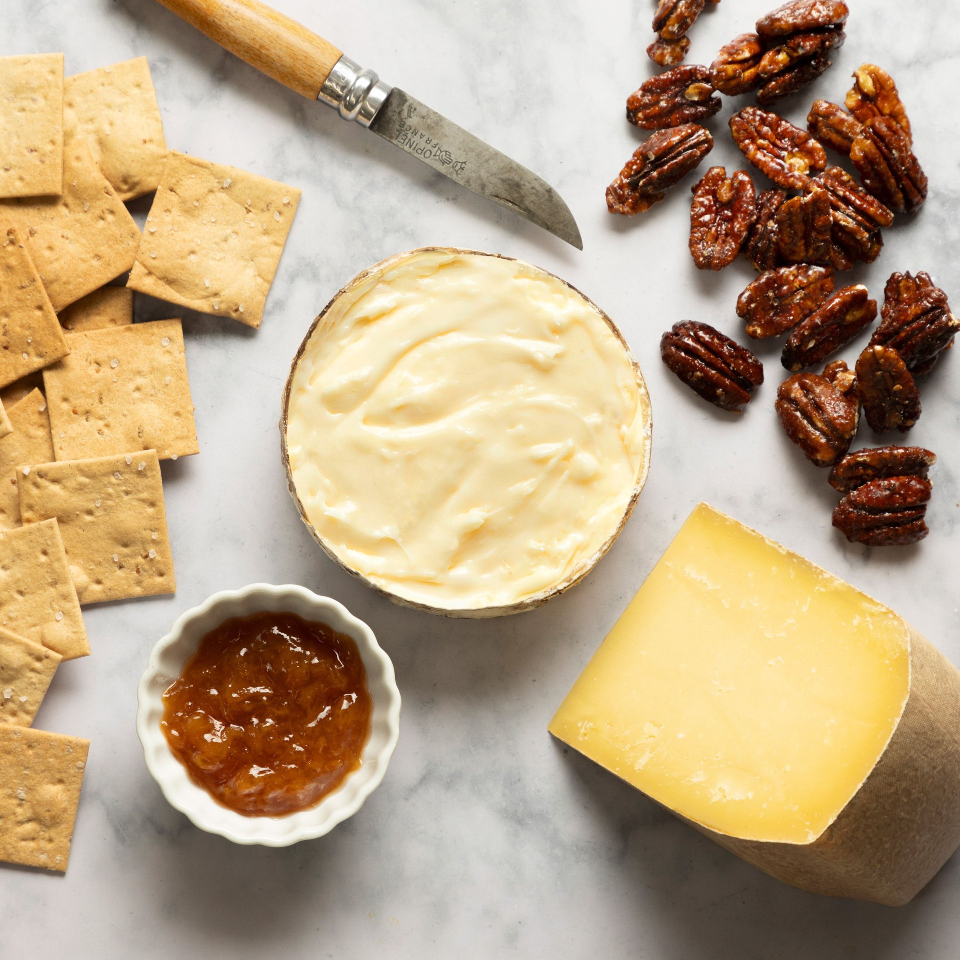 The Everything & More gift box spread on marble: Pleasant Ridge Reserve, Rush Creek Reserve, crackers, candied pecans and honey