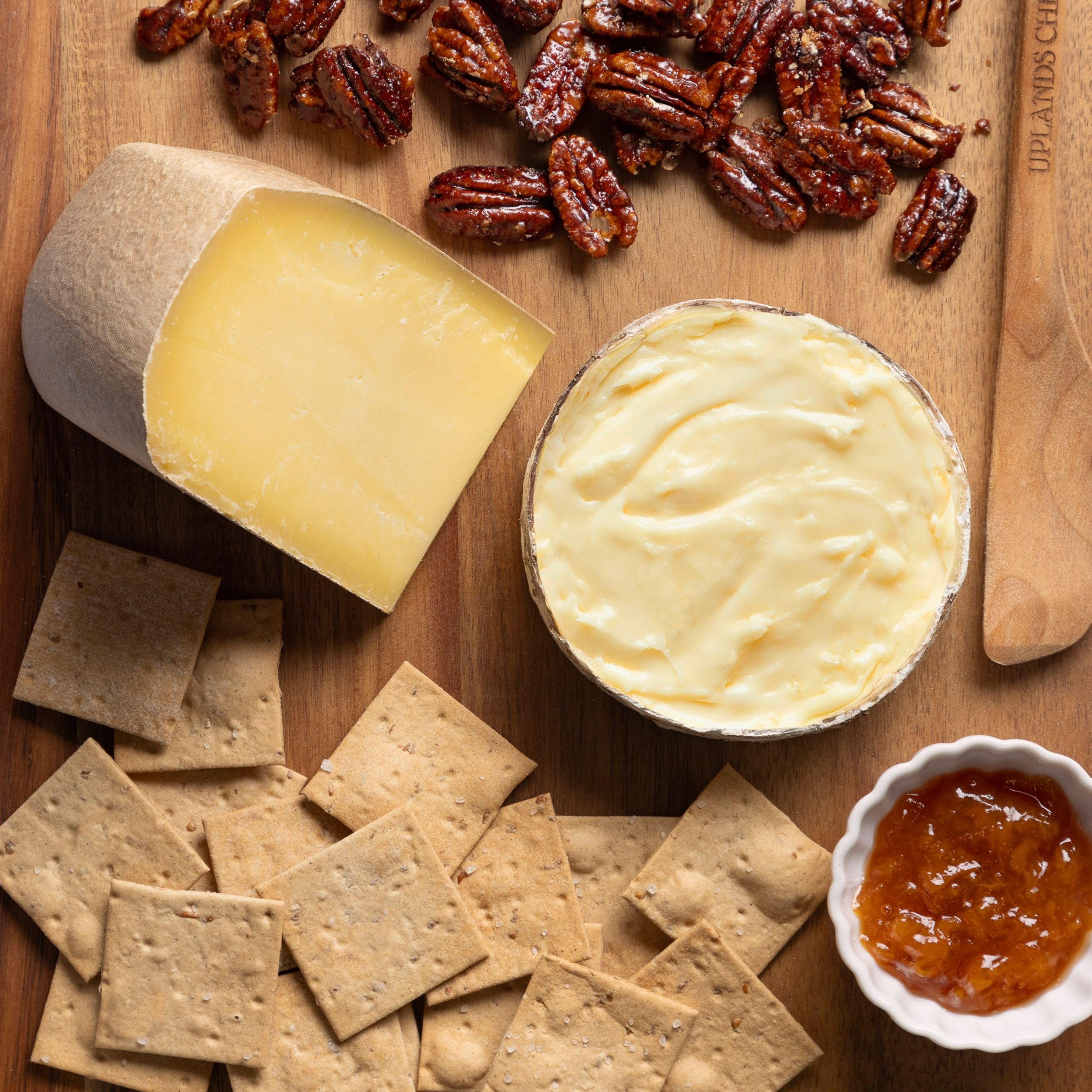 The Everything & More gift box spread on a wooden board: Pleasant Ridge Reserve, Rush Creek Reserve, crackers, candied pecans and honey