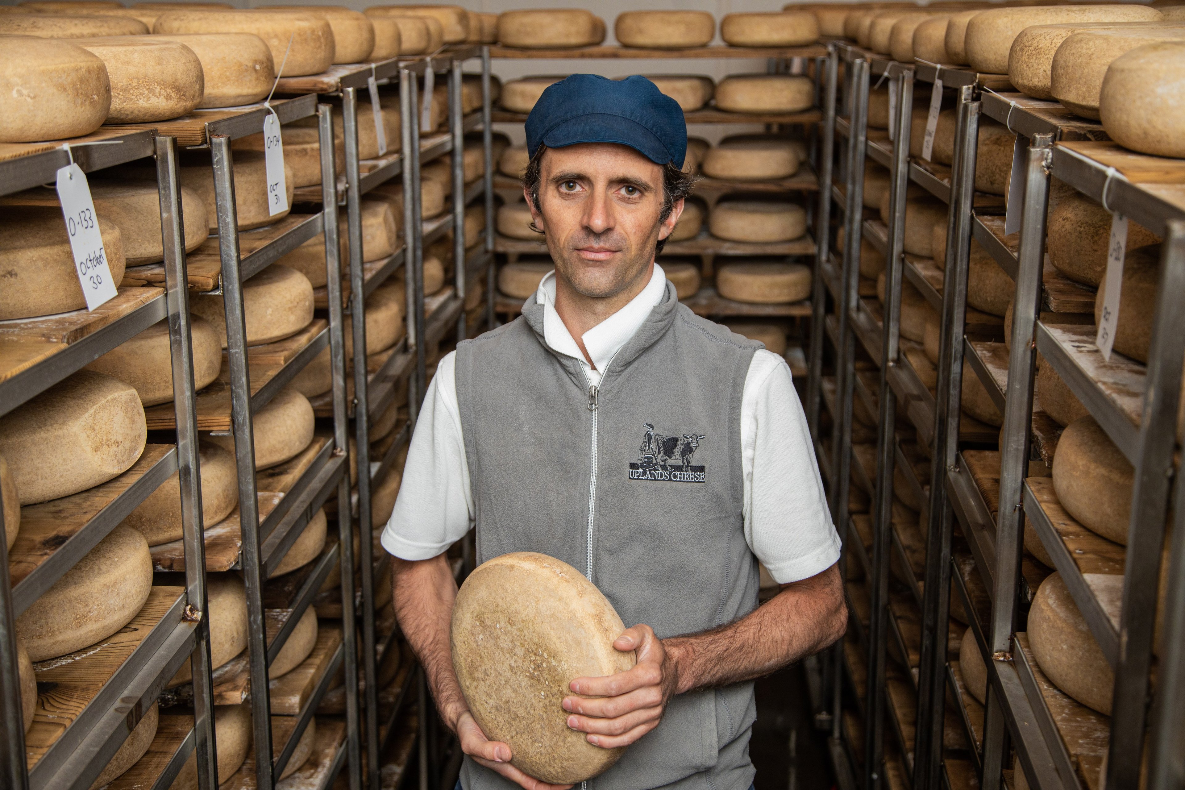 Andy Hatch holding a wheel of Pleasant Ridge Reserve among the cave's aging shelves