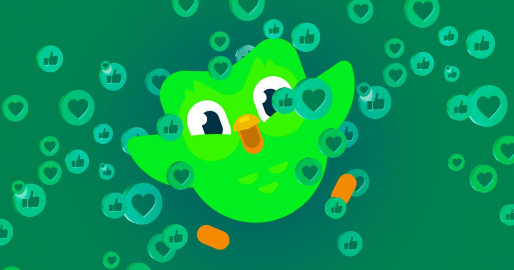 Duo, the green Duolingo owl, surrounded by floating heart and thumbs-up icons on a green background.
