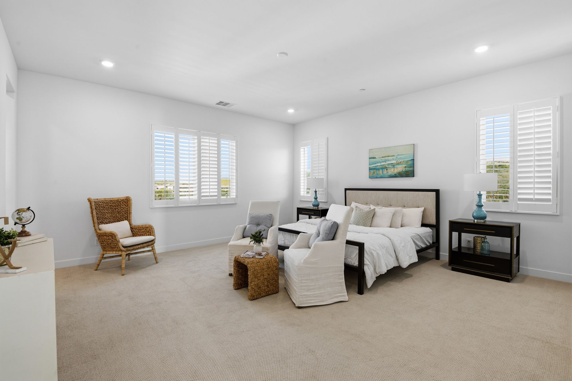 A bedroom with a plush bed, two light upholstered chairs, and natural light through shutters