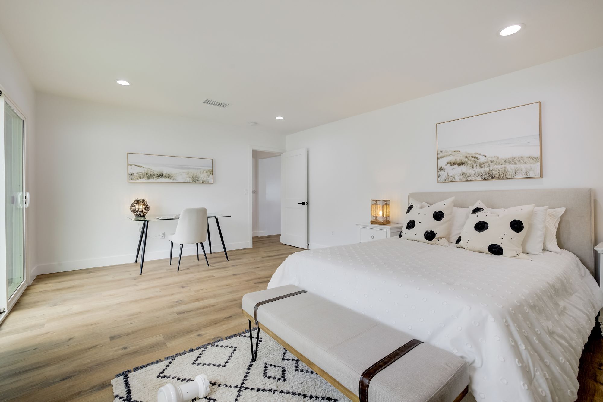 A bedroom with patterned pillows, a desk, and large glass doors