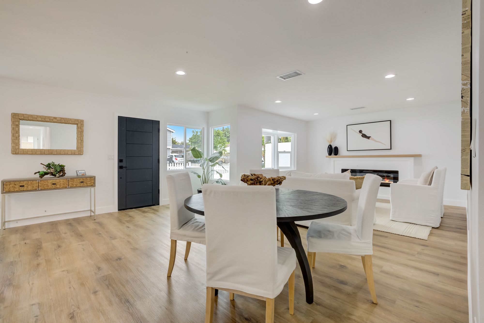 A living area with a round black dining table, white chairs, and large windows