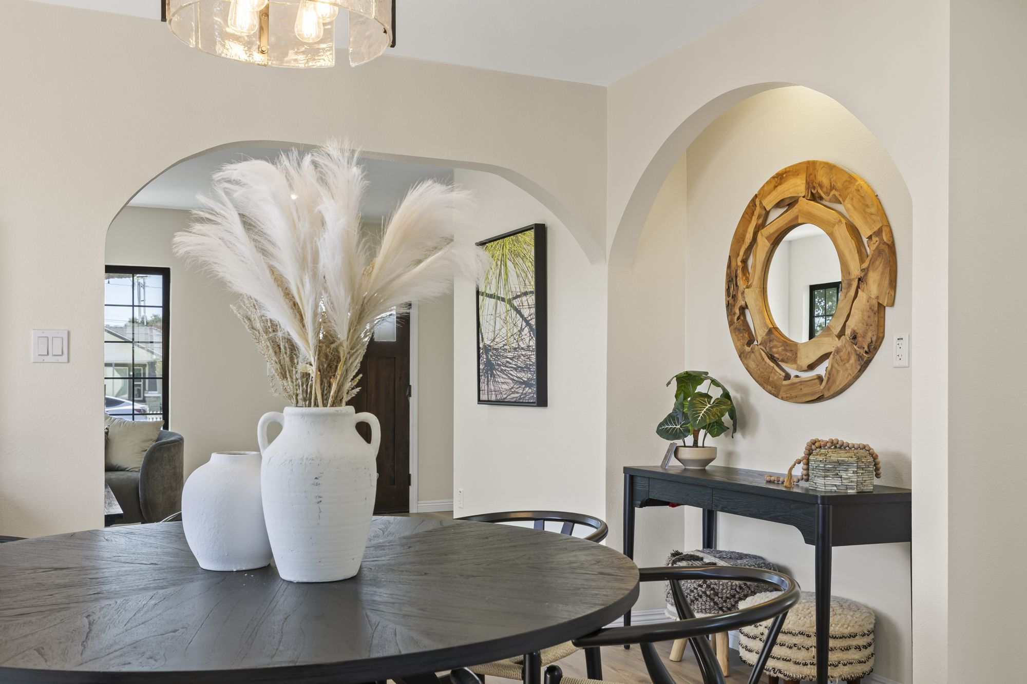 A dining area with a round table, black chairs, pampas grass centerpiece, and a wooden mirror