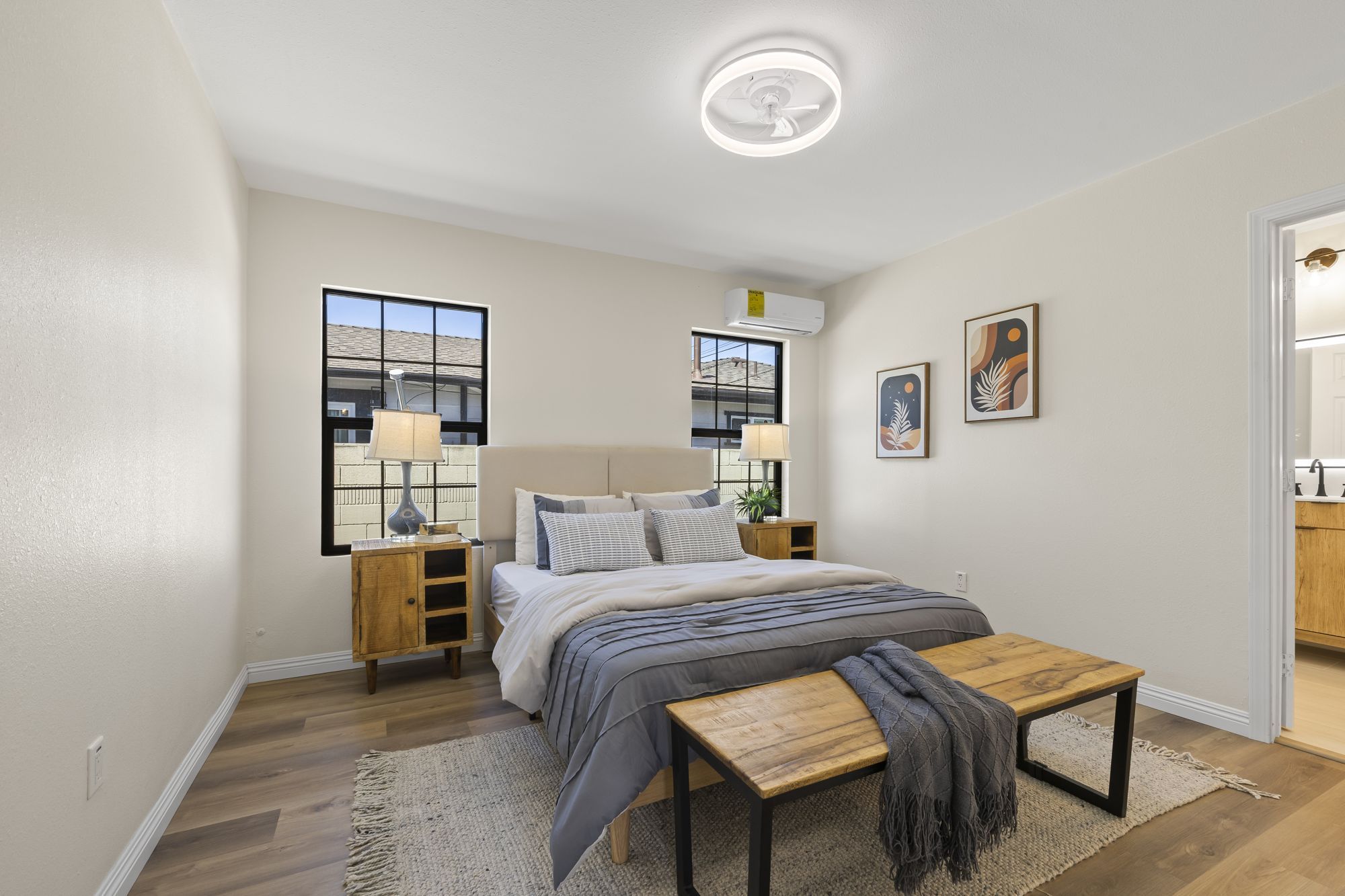 Contemporary bedroom with a light color scheme, cozy bed, wooden nightstands, and large windows
