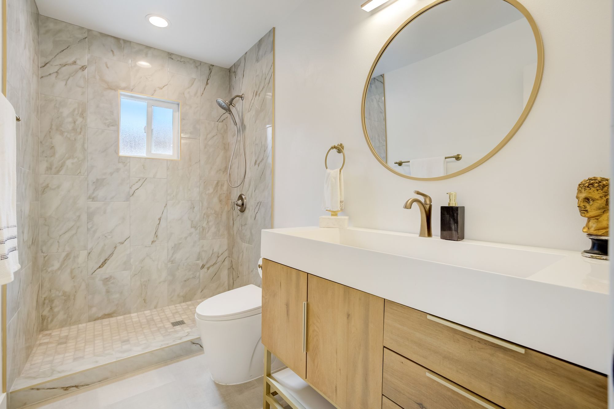 A modern bathroom with marble walls, a wooden vanity, and a round mirror