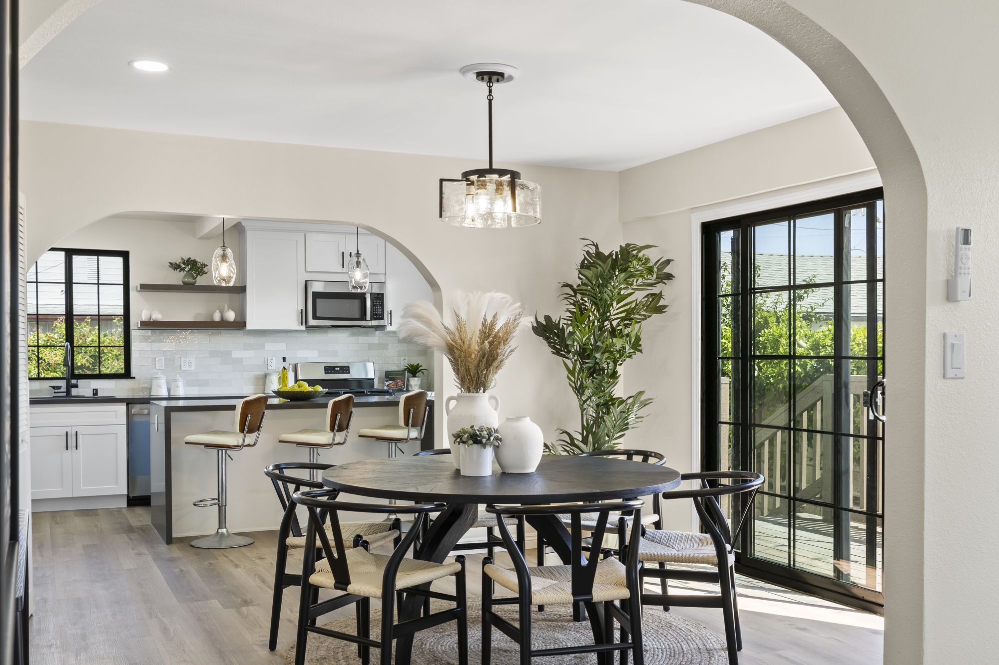 A modern dining area with a round black table and woven chairs, leading to a contemporary kitchen