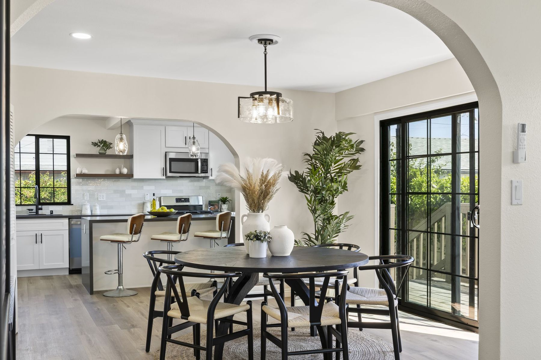 A Santa Ana dining room seen through an arched opening, with a round black table and woven chairs