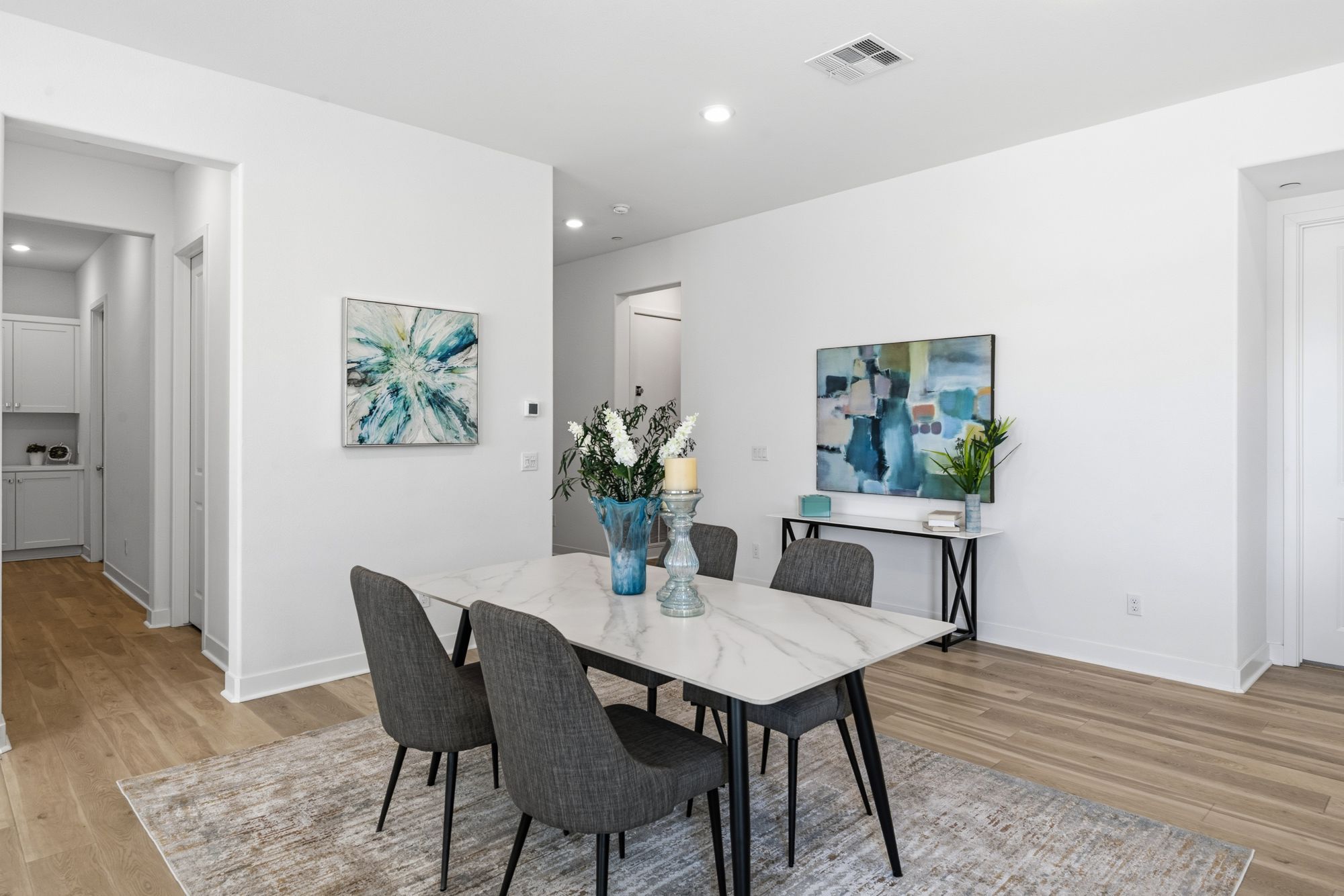 A modern dining area with a marble table, gray chairs, a floral arrangement, and abstract paintings