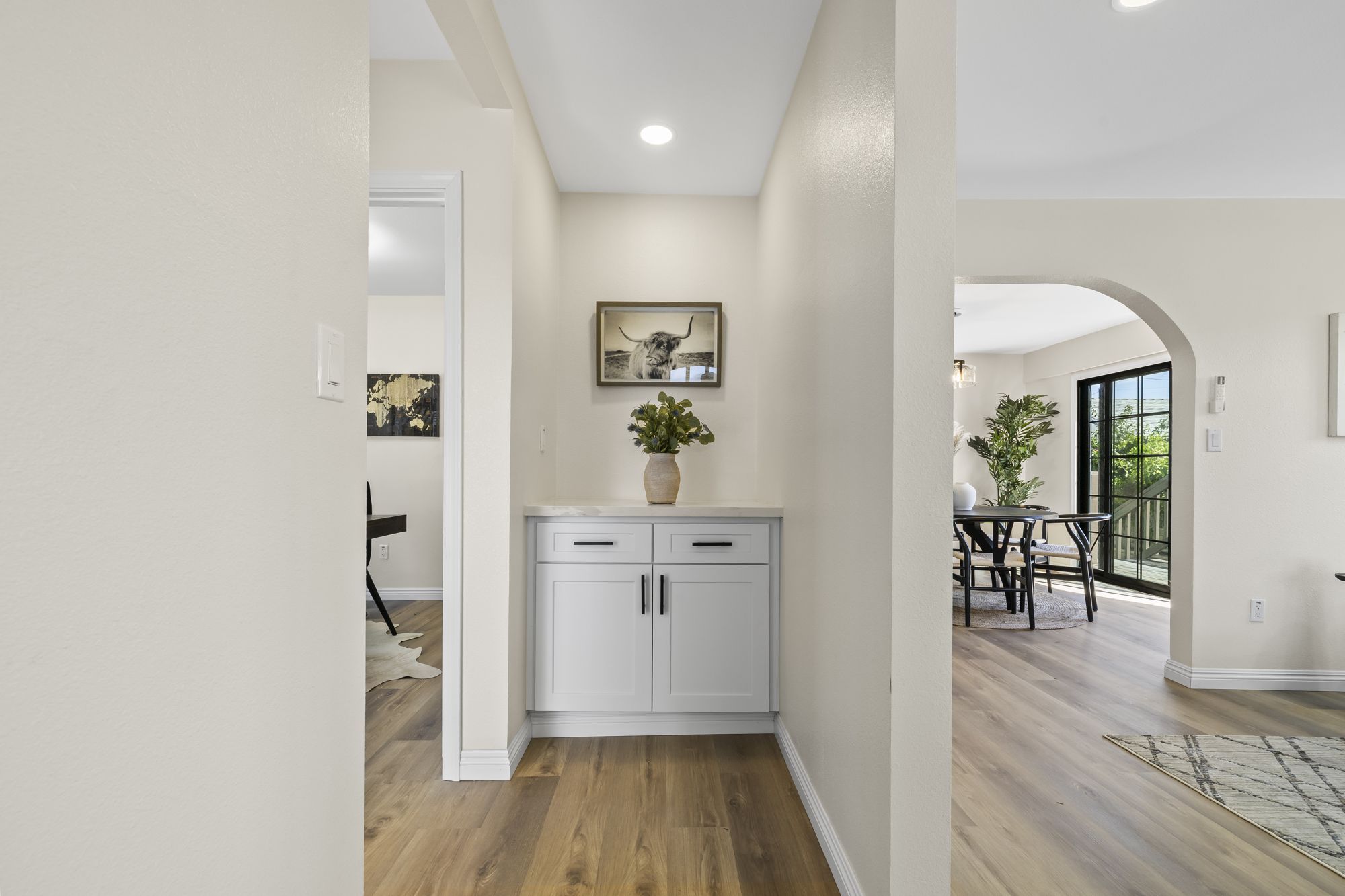 A modern entryway with a white cabinet, a vase of greenery, and an arched doorway leading to a dining area