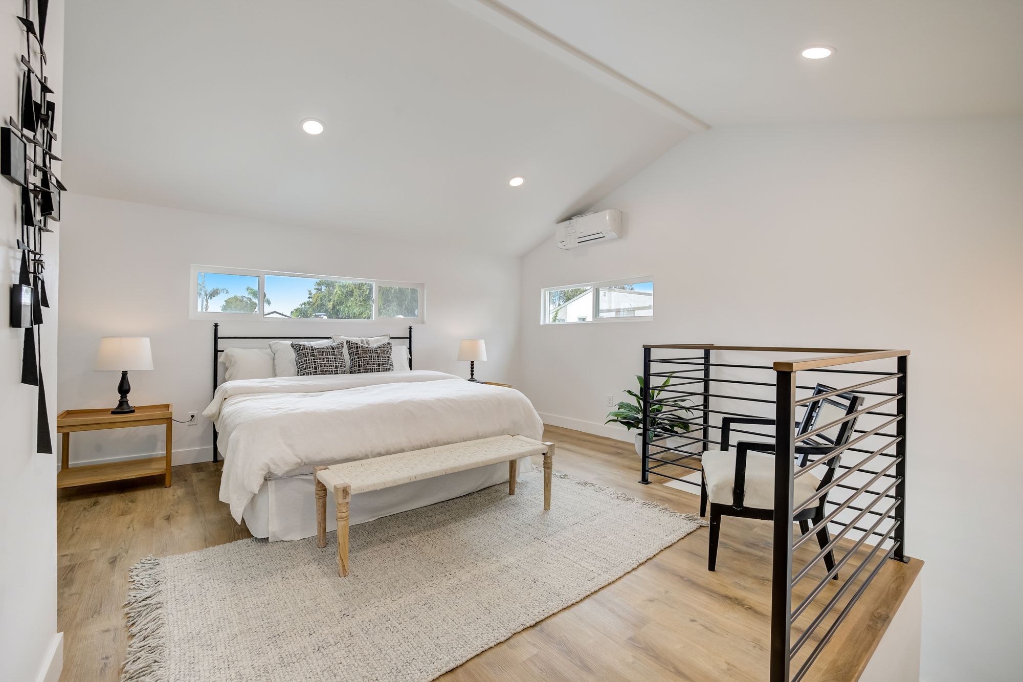 A bedroom with a black metal bed, white linens, and large windows
