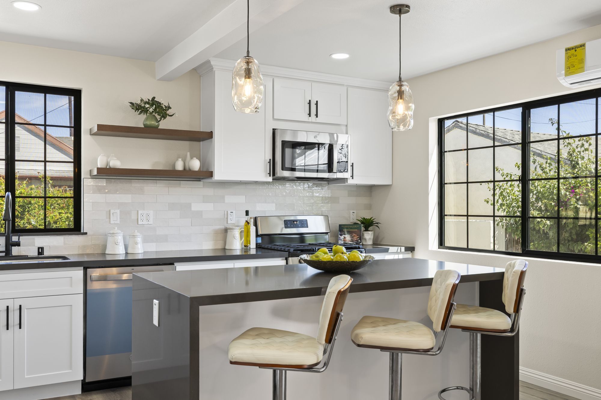 Modern kitchen with white cabinetry, stainless steel appliances, and a dark countertop island with bar stools