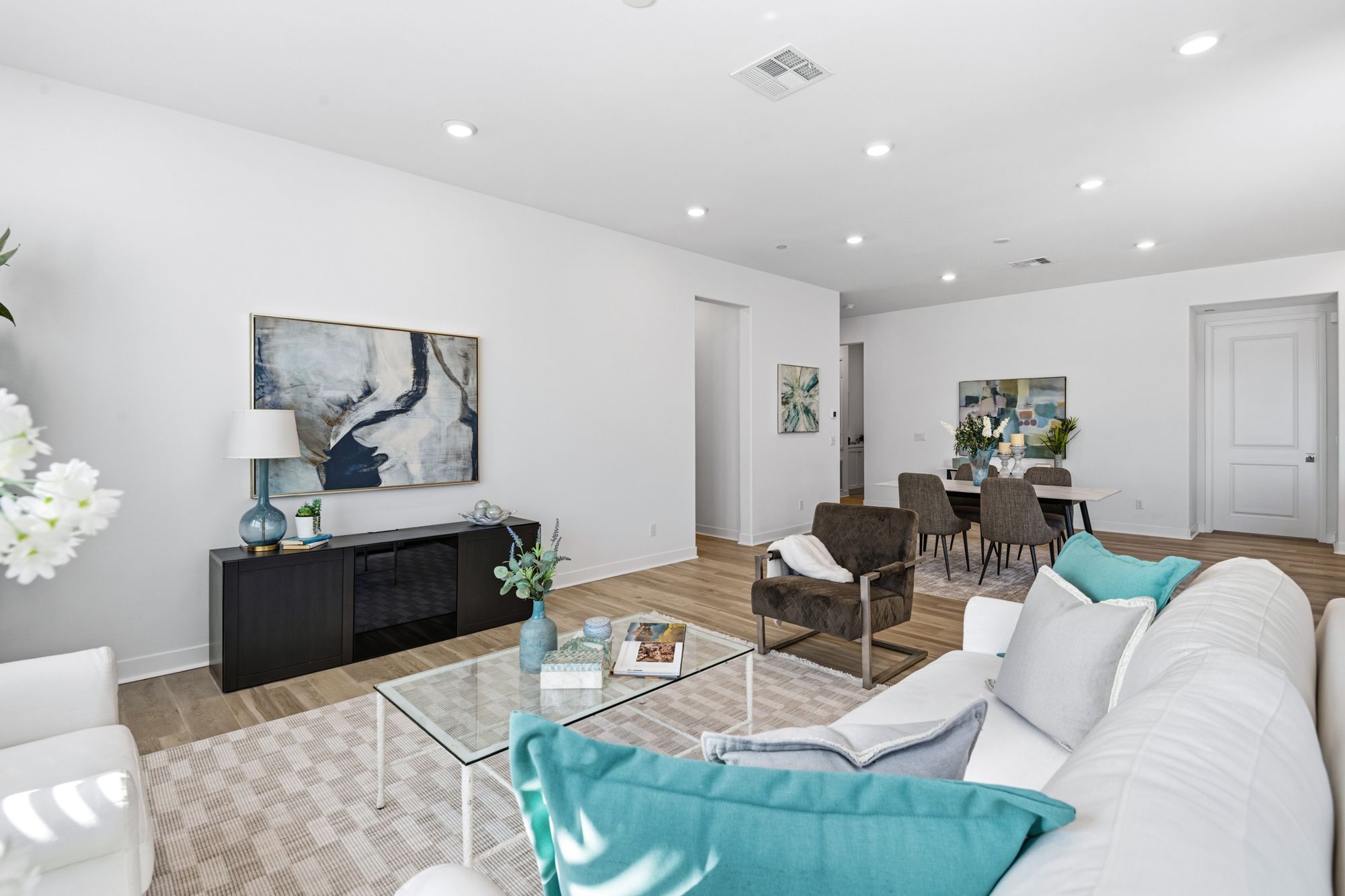 A modern living room with a light leather sofa, turquoise cushions, a glass coffee table, and contemporary art