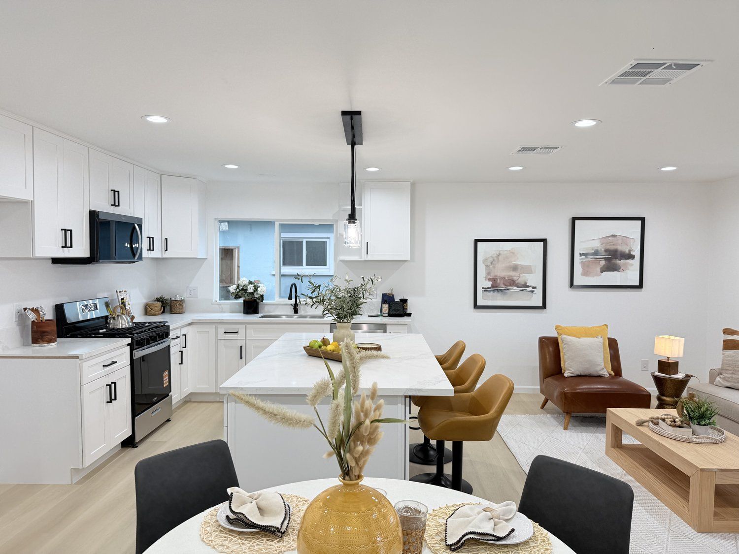 A kitchen and dining area with white cabinetry, a marble countertop, and warm tan furniture