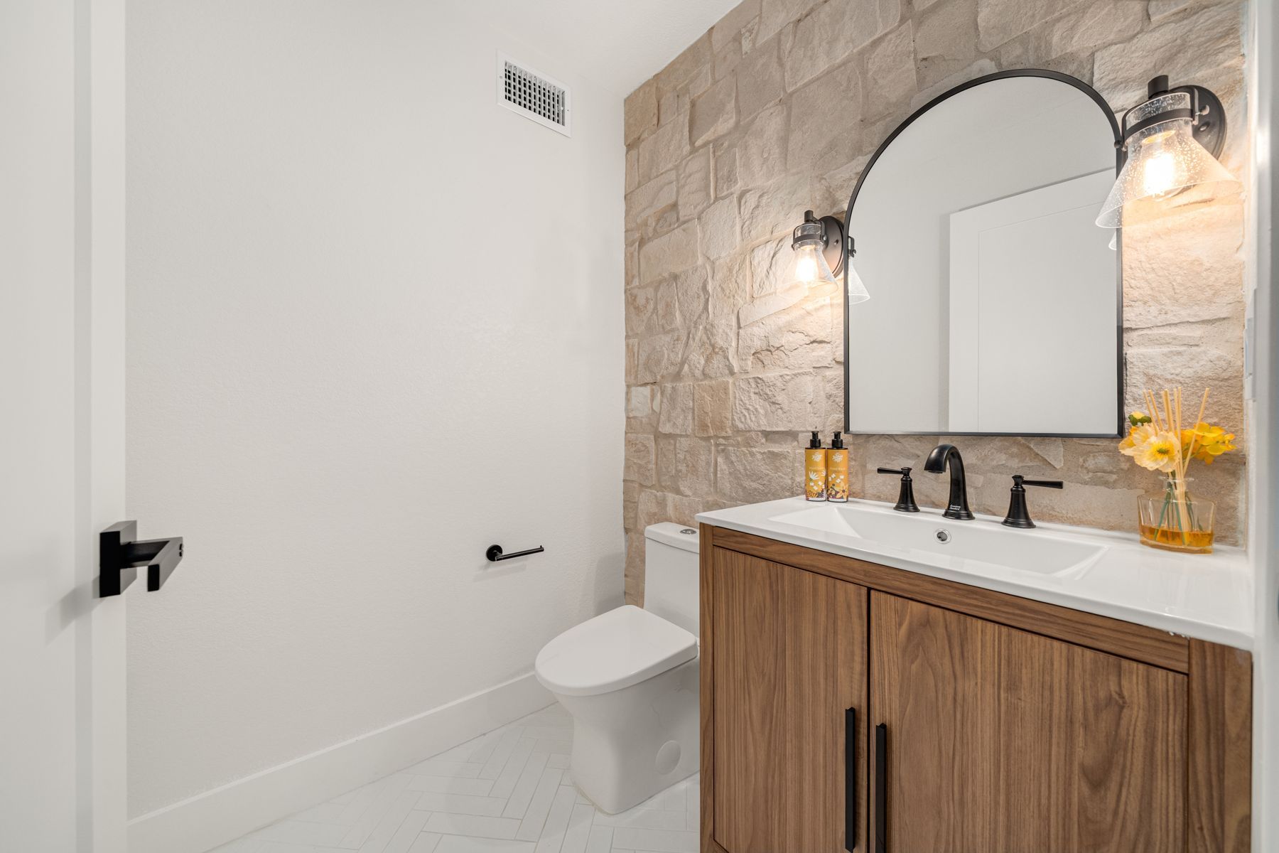 A modern bathroom with a stone accent wall, wooden vanity and round mirror