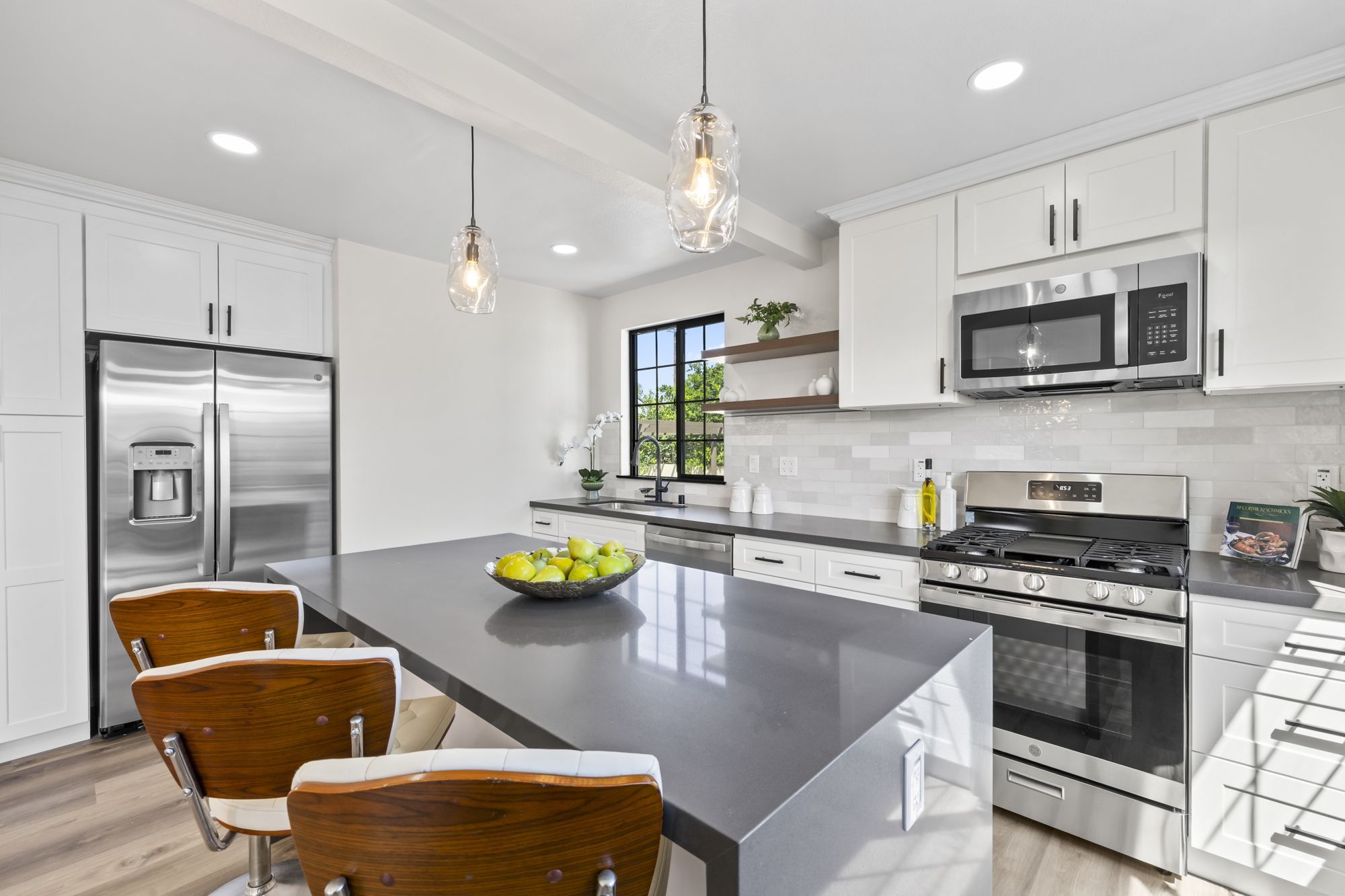 Modern kitchen with white cabinets, gray countertop, and a bowl of green apples under pendant lights