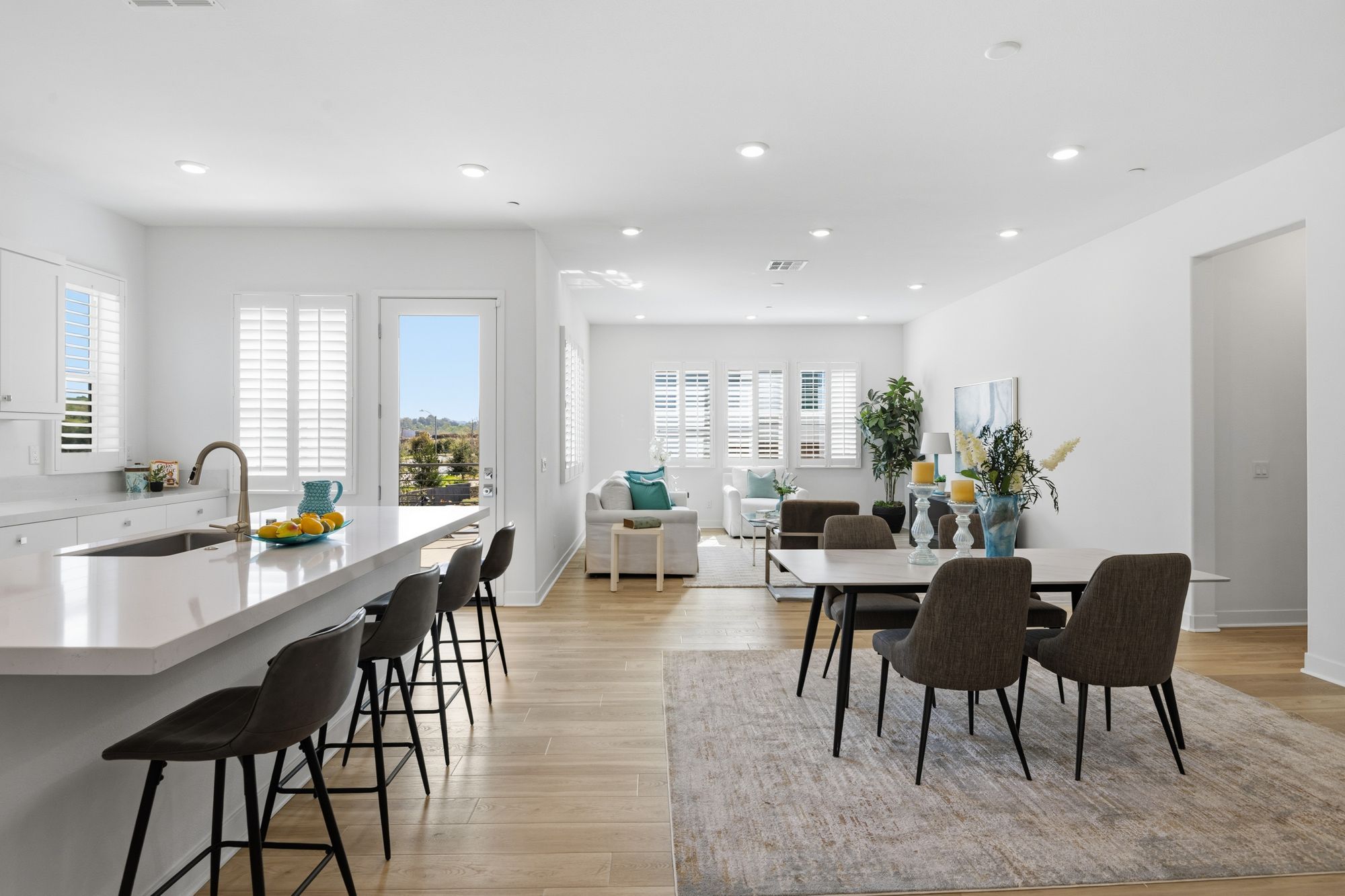 Open family living space with a white kitchen, bar seating, dining area, and teal accents