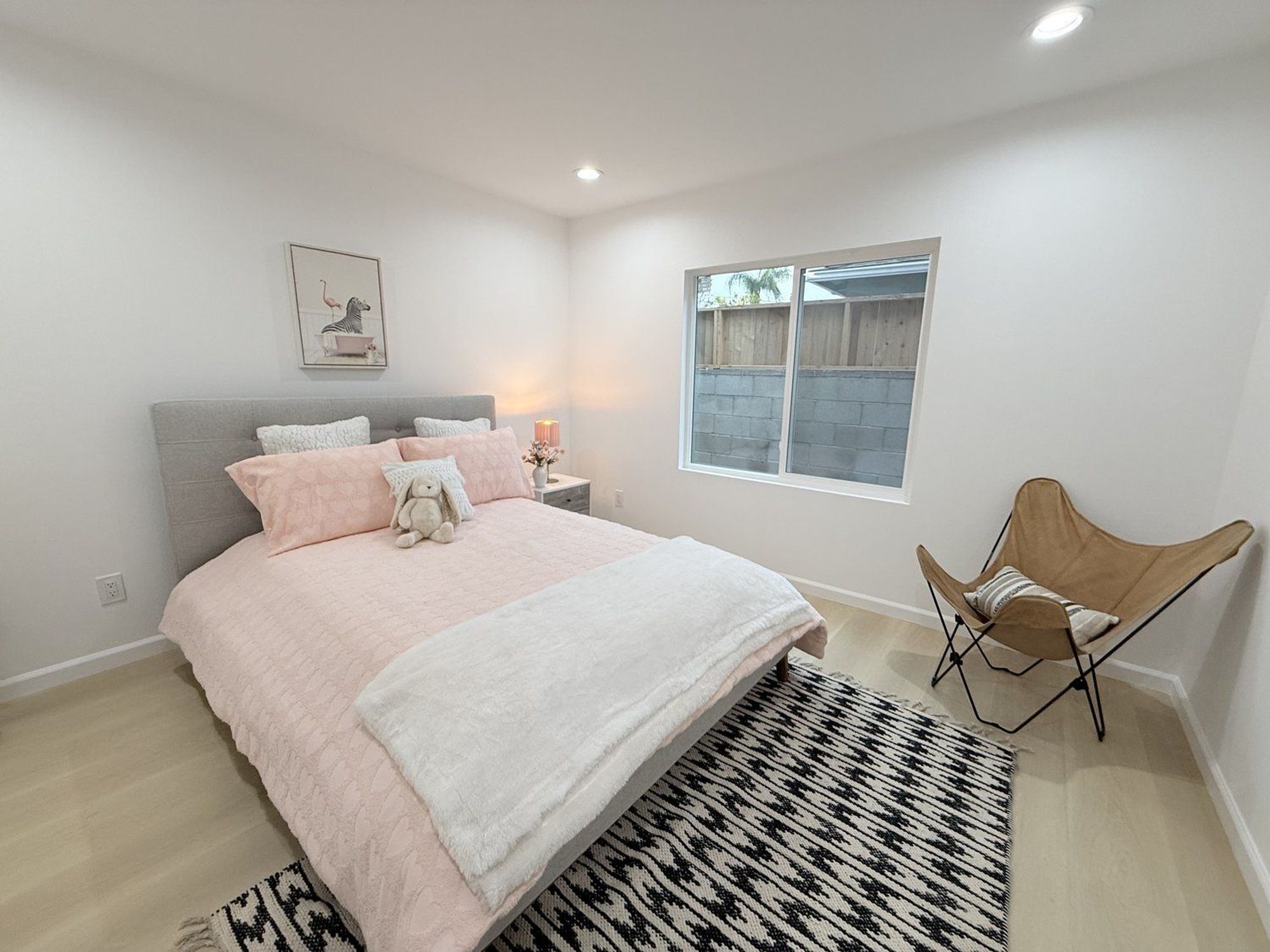A bedroom with a pink quilted bedspread, accent pillows, a cozy chair and a rug