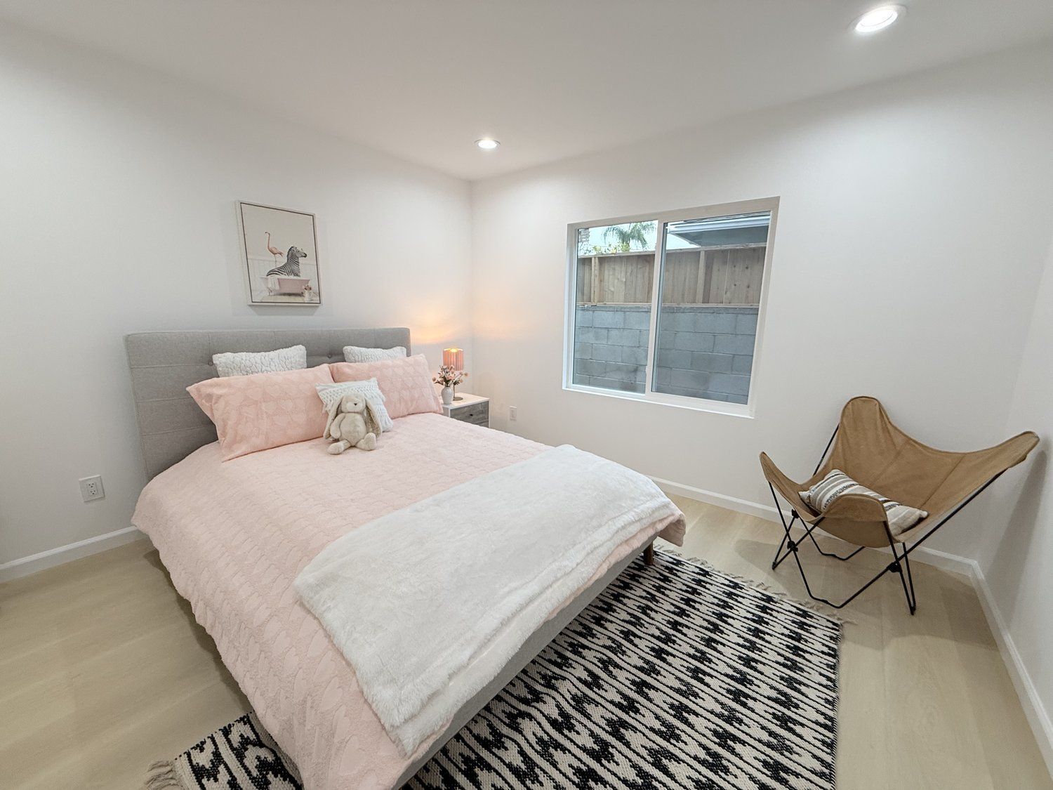 A bedroom with a pink quilted bedspread, accent pillows, a cozy chair and a rug