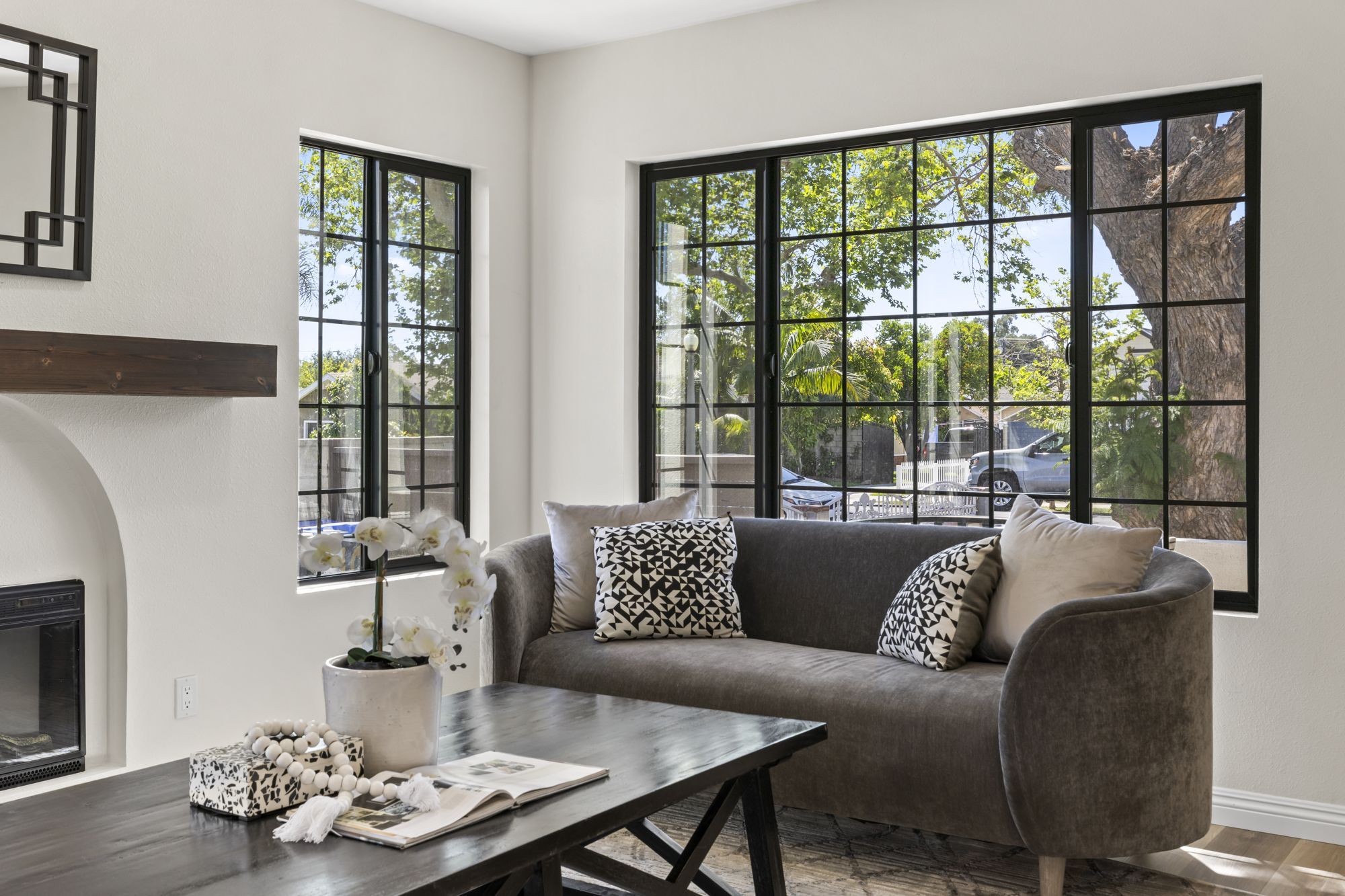 A contemporary living room with a gray sofa, patterned pillows, and large windows letting in natural light