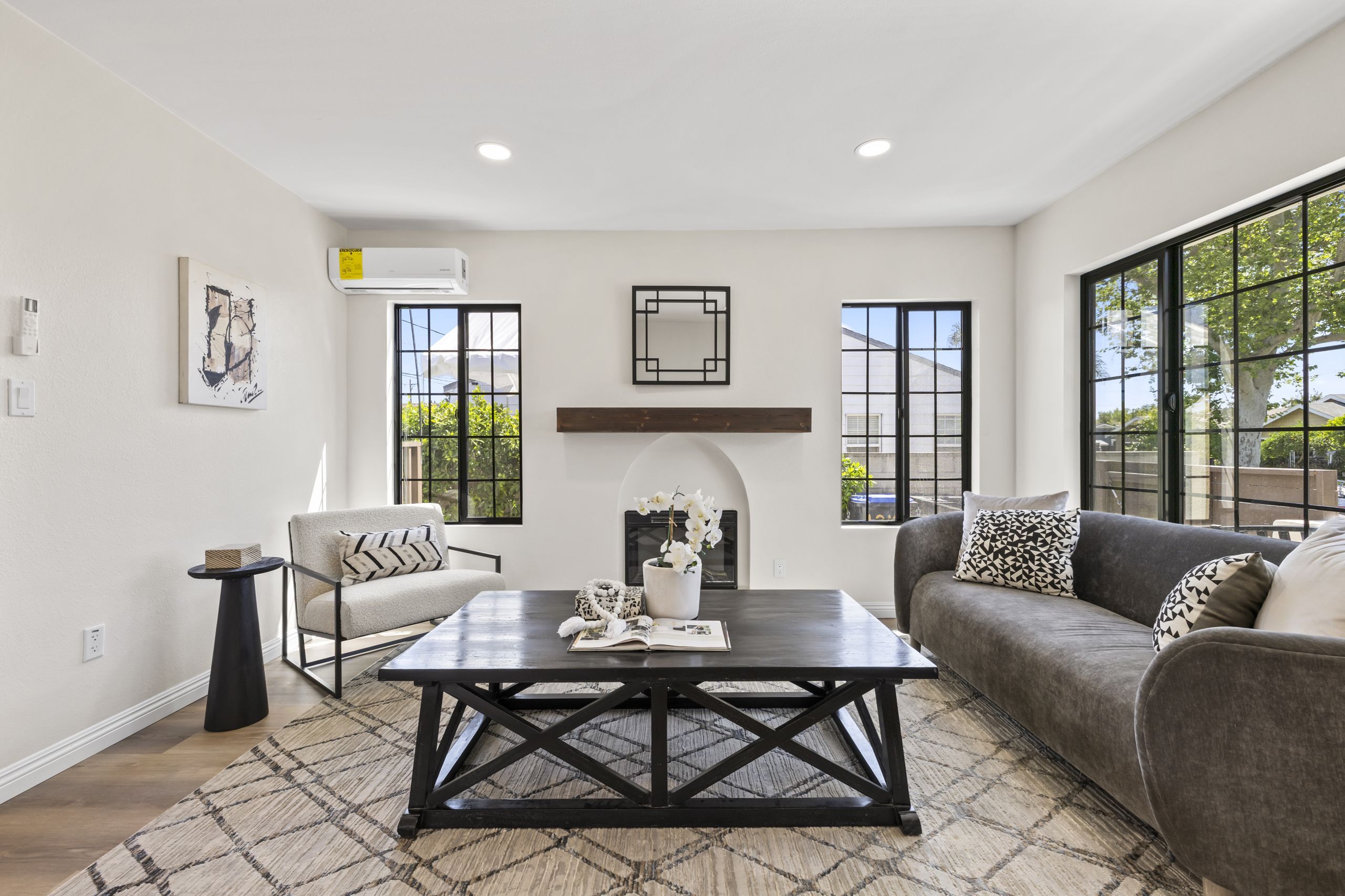 A staged living room in Santa Ana with a gray curved sofa, black coffee table, patterned rug and arched fireplace