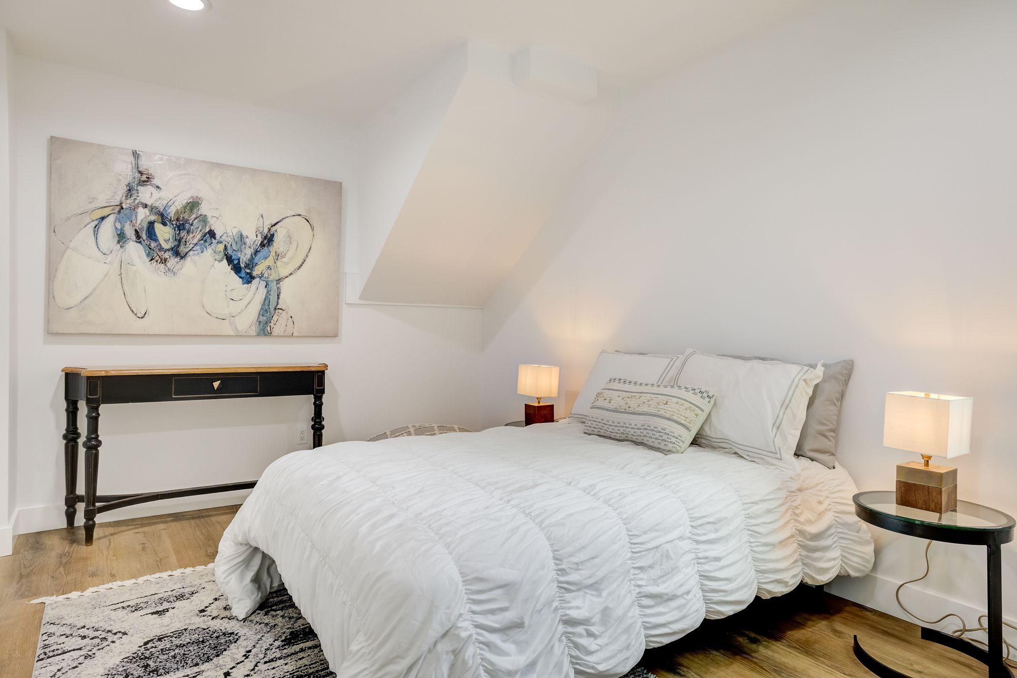A bedroom with a white bedspread, abstract art, and warm bedside lamps