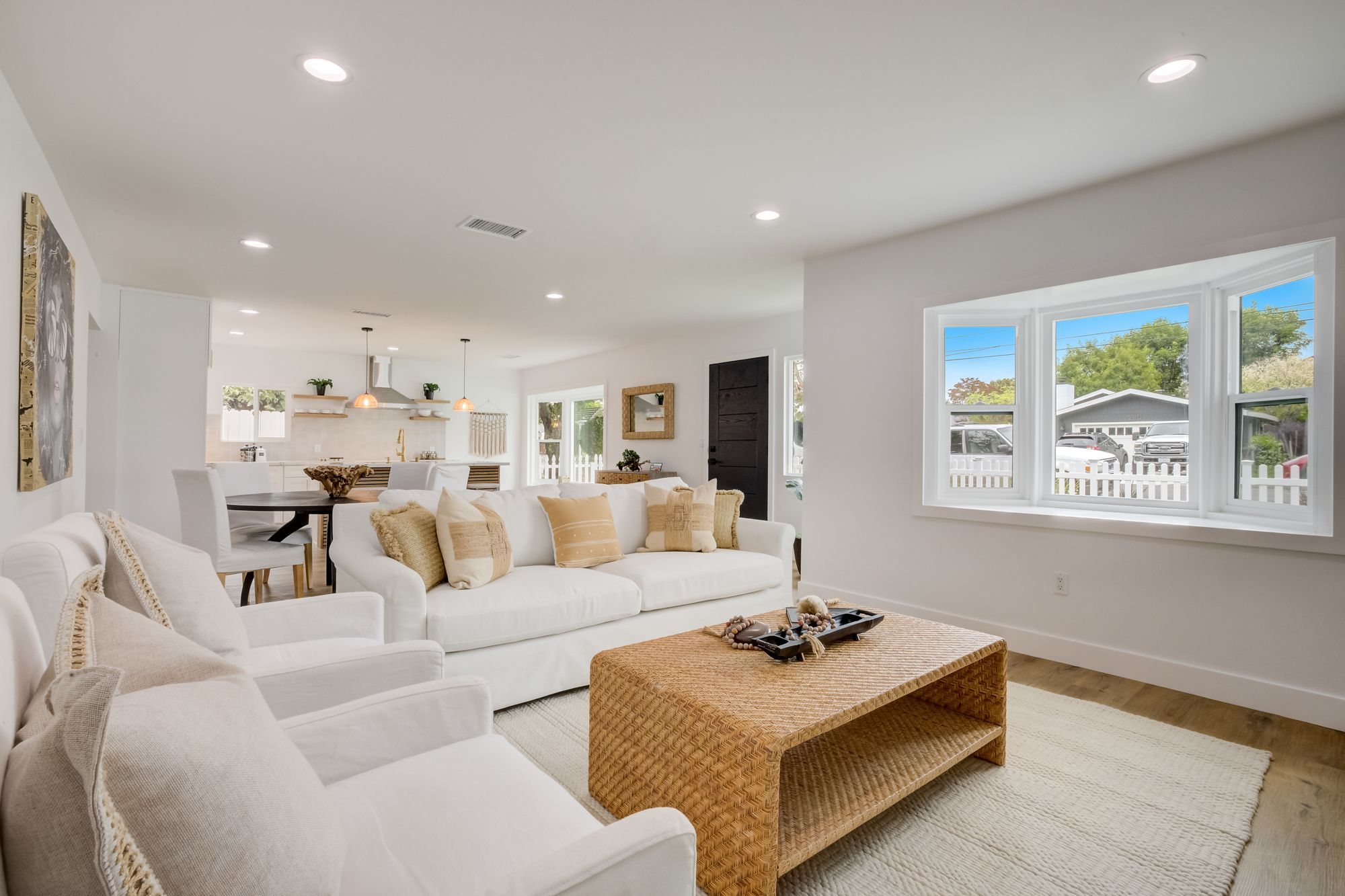 Bright living area with a white sectional sofa, woven coffee table, and large windows