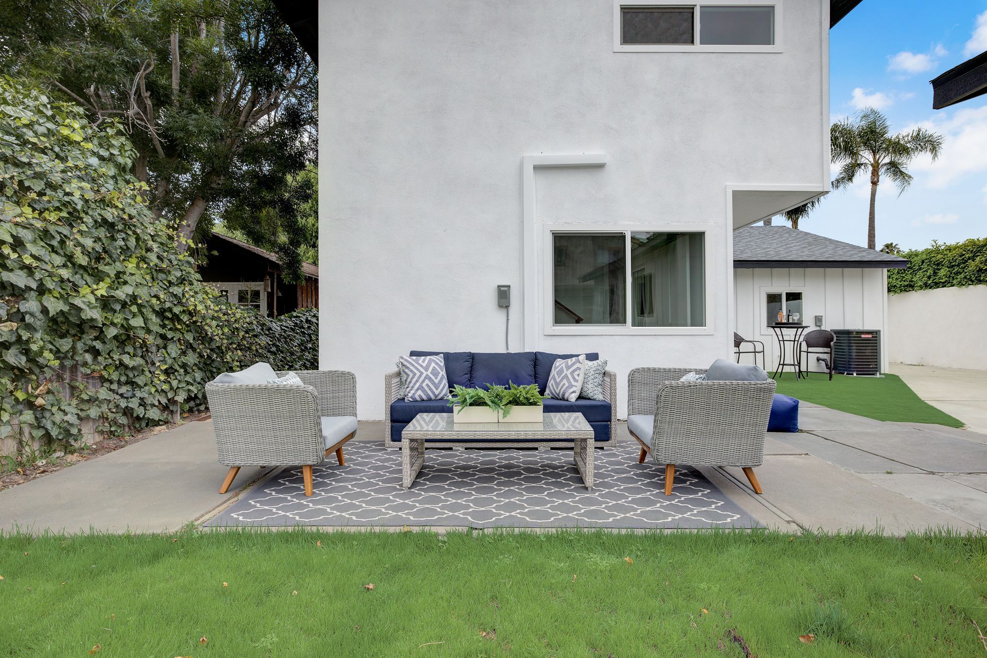 An outdoor seating area with a navy sofa, light gray armchairs, and a glass coffee table