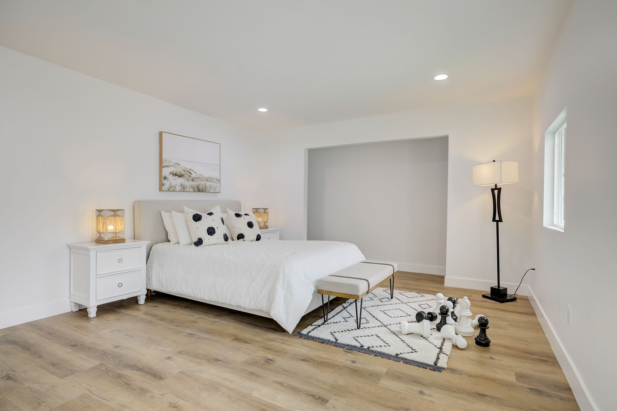 A bedroom with a queen bed, geometric rug, accent bench, and decorative chess pieces