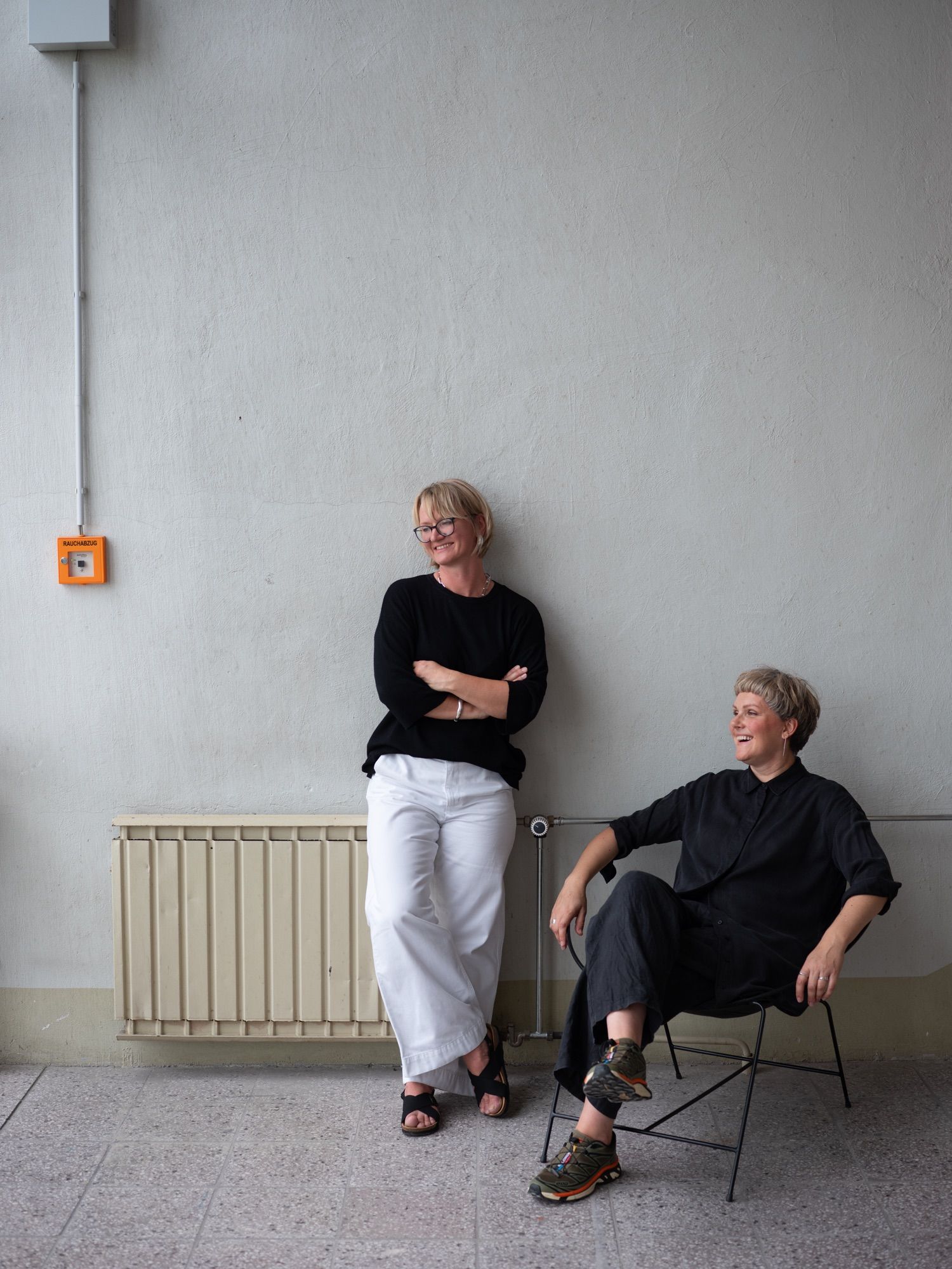 The two founders against a studio wall, one standing, one seated in a Circle chair.