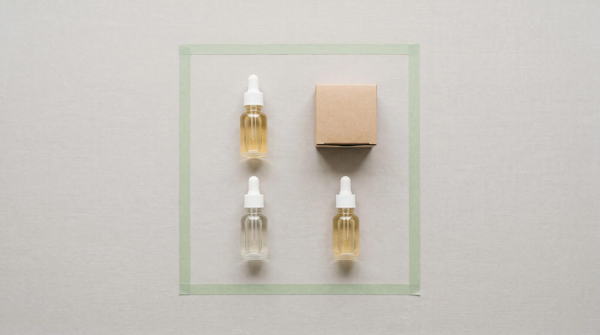 Overhead still life of glass bottles and a small box arranged in a tidy grid inside a square outline of pale green tape