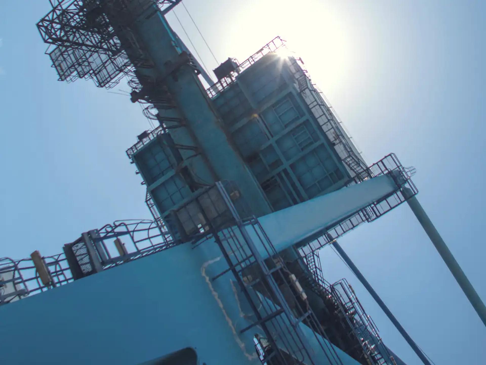 A quay crane at the Port of Mombasa seen from below, the sun behind its machinery house
