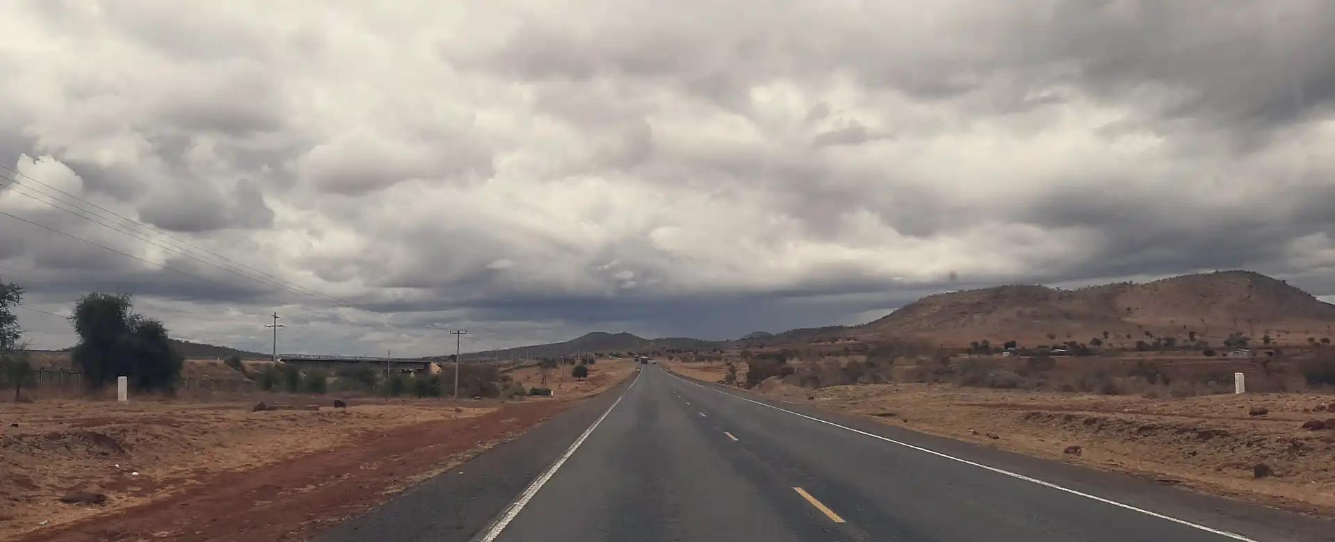 An empty two-lane highway running into dry hills under grey cloud