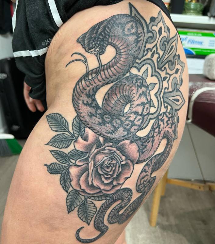 Tattoo of a coiled snake with a rose on thigh.