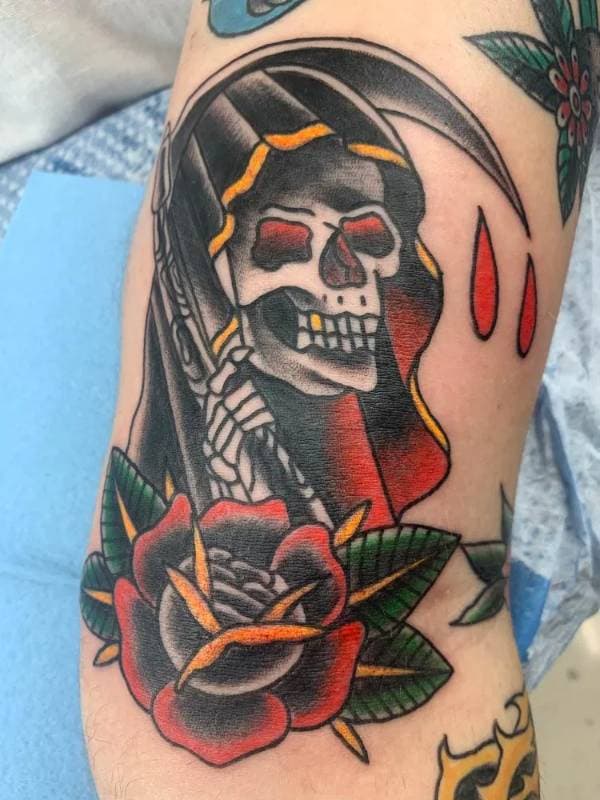 Tattoo of a reaper and rose in American Traditional style on forearm.