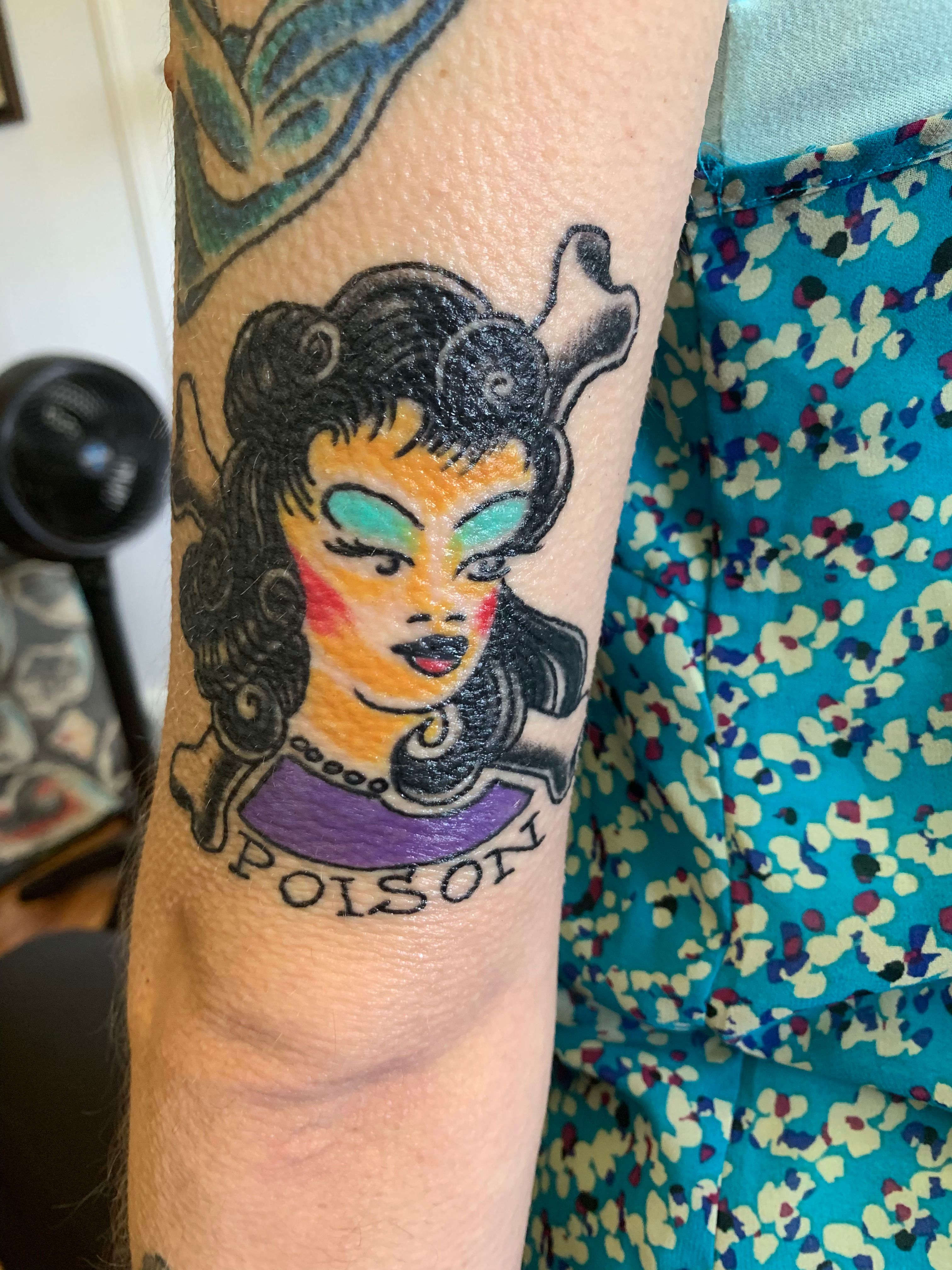 Tattoo of a woman with the word 'Poison' on the forearm.