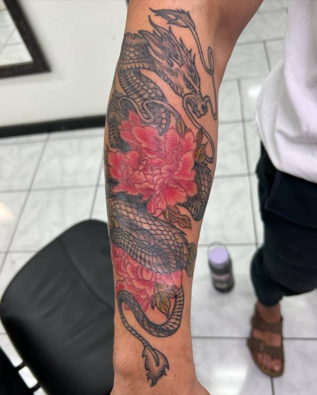 Forearm tattoo featuring a Japanese dragon with red peonies.