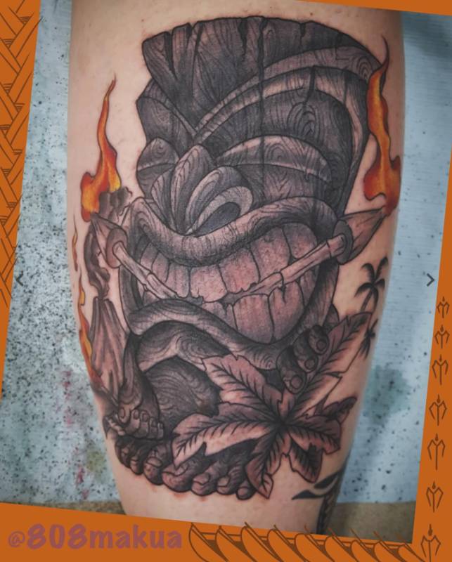 Tattoo of a tiki mask with flames on a thigh.