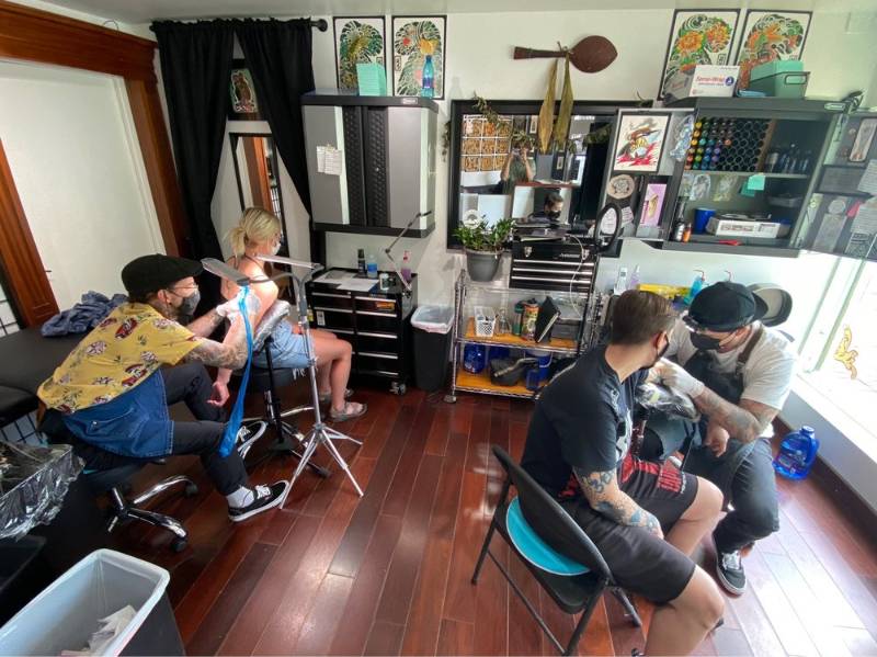 Tattoo artists working on two clients inside a bright tattoo studio.
