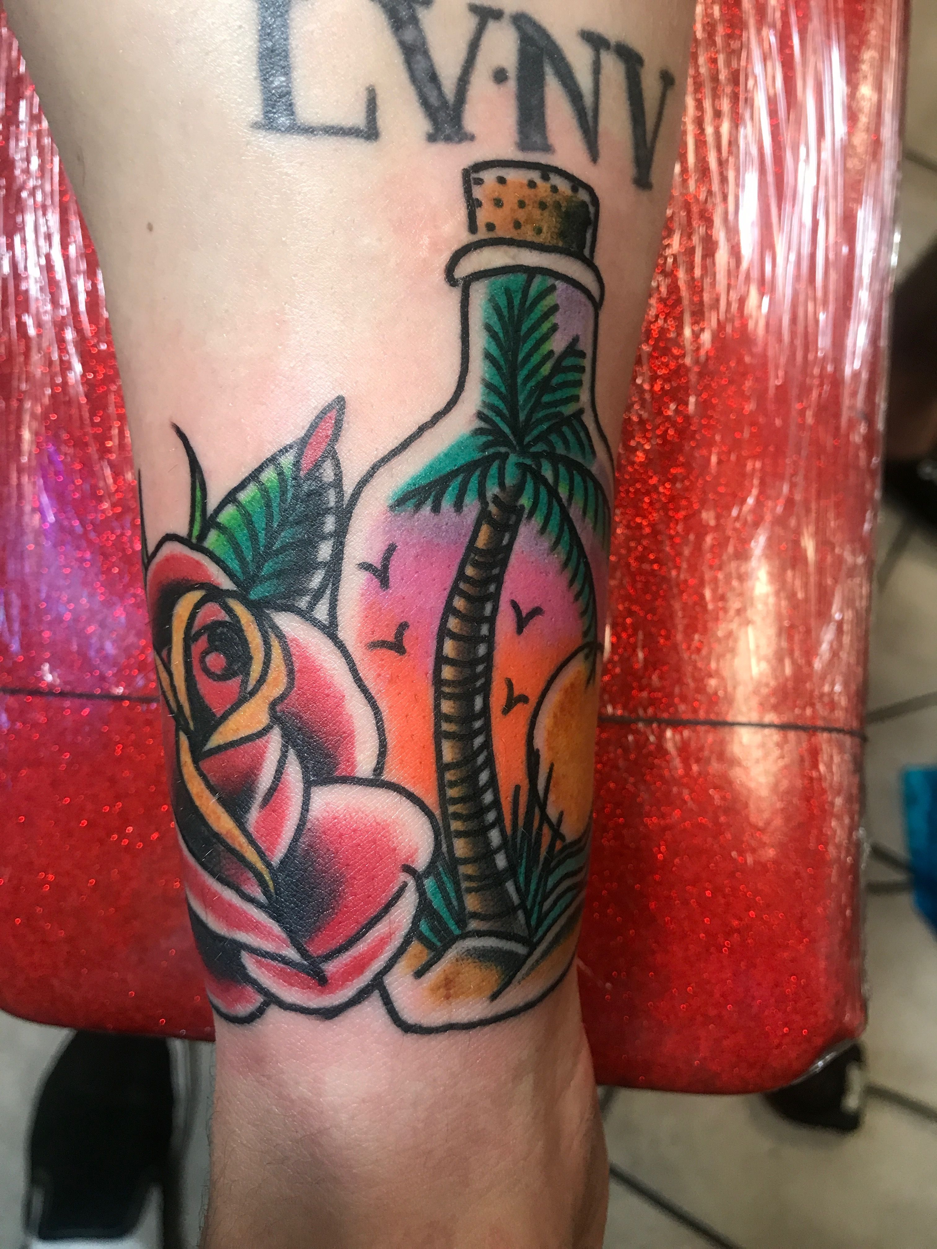 Tattoo of a rose and palm tree in a bottle on forearm.