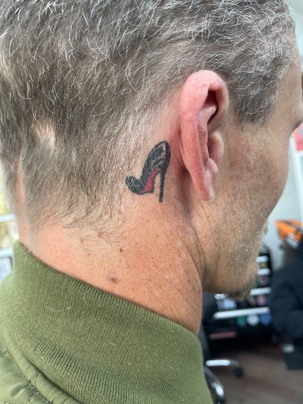 Small high-heeled shoe tattoo behind ear.