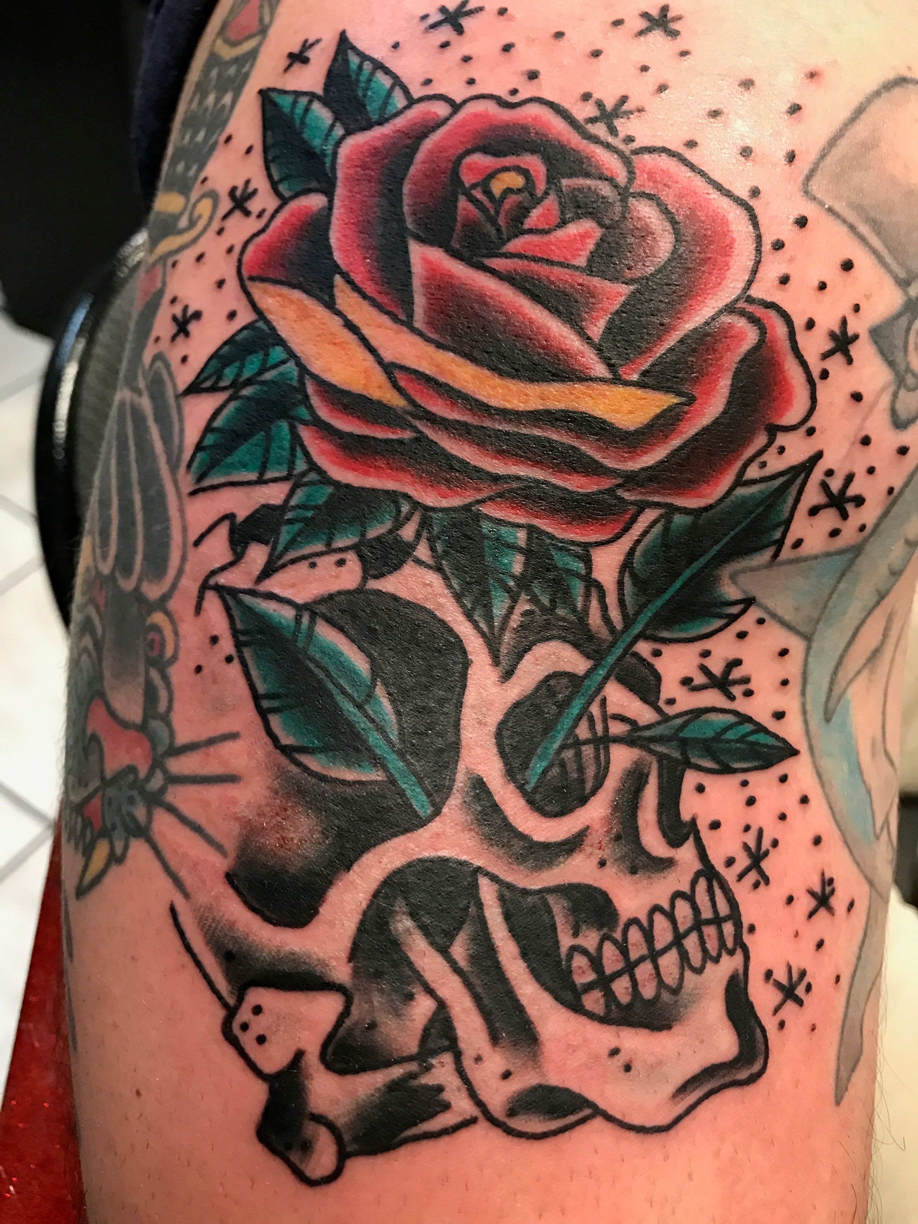 Colorful tattoo of a rose and skull on an upper arm.