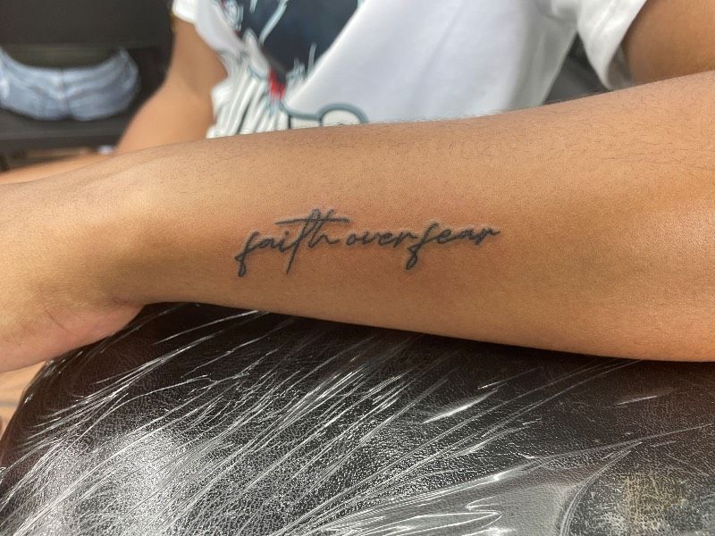 Tattoo of the words 'faith over fear' on a forearm.