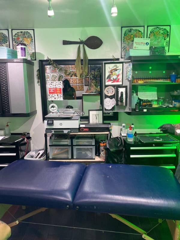Tattoo studio workstation with a tattoo bed, equipment, inks, and wall art.
