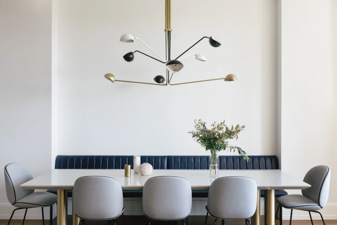 Large dining table with banquet seating against the wall and 5 additional chairs under multi-light pendant fixture