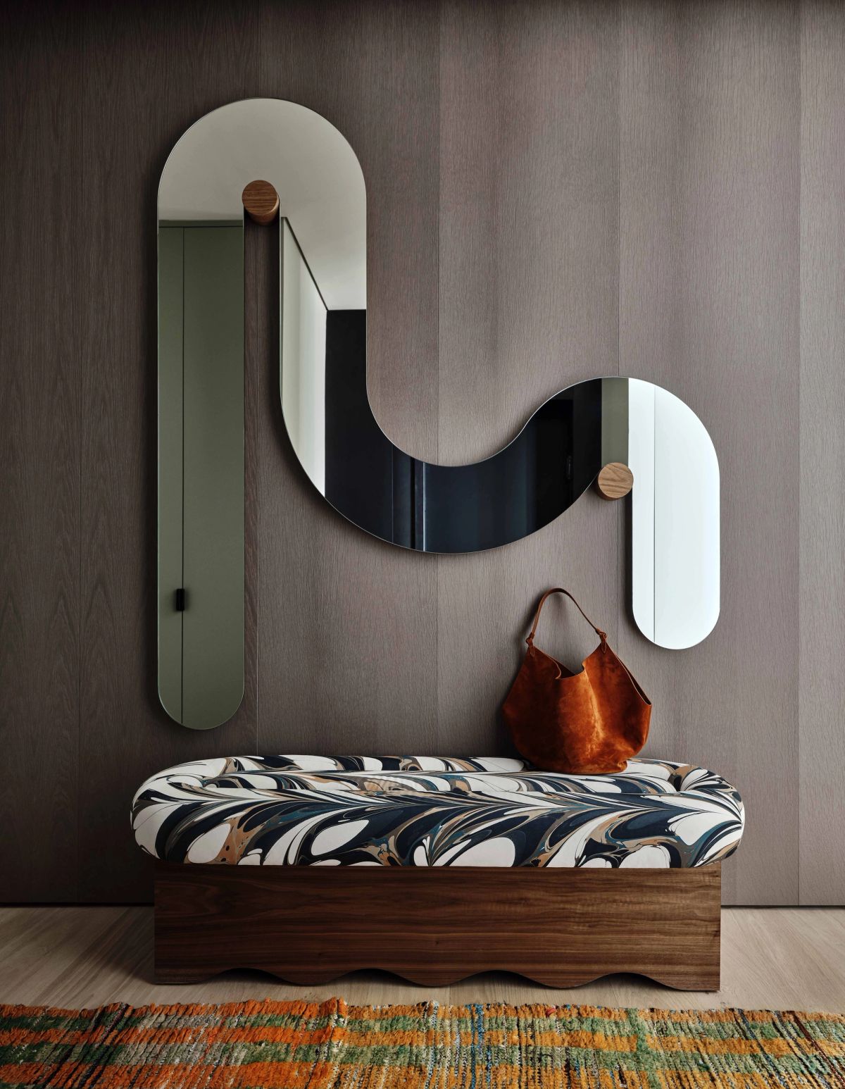 Uniquely-shaped mirror hangs in the foyer abov bench with hand-painted seat cover