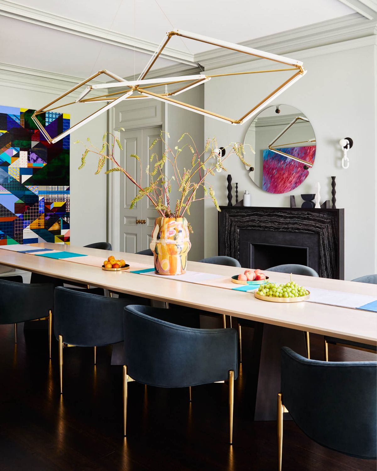 Custom dining table with geometric chandelier above, fireplace with mirror and sconces above