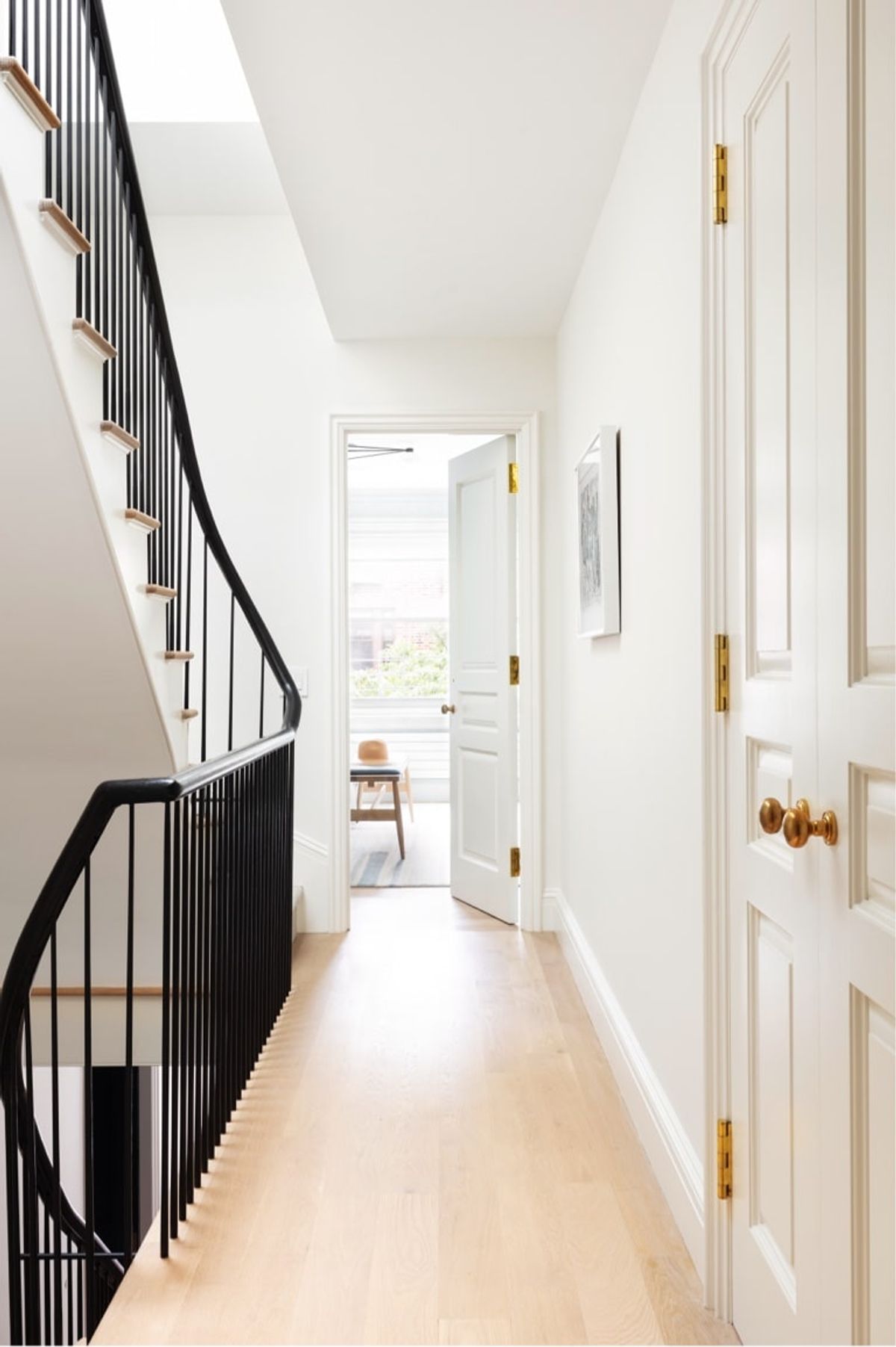 Upstairs hallways with white walls, black stairwell and light colored wood flooring