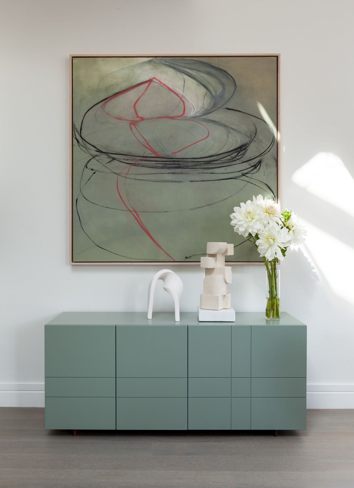 Artwork hangs over sage green modern credenza